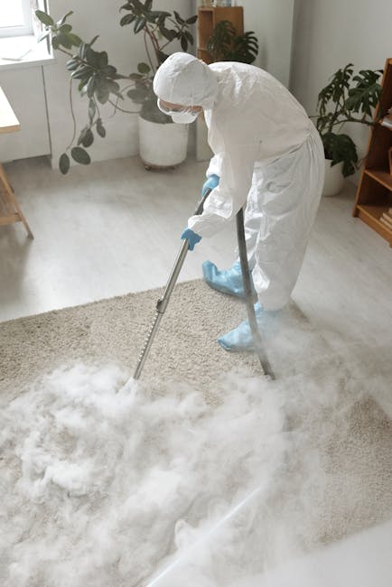 A woman with curly hair, wearing a beige jacket, dark jeans, and white shoes, engages in surface cleaning using a yellow vacuum cleaner with a black hose in a living room. The room features a wooden f